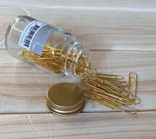 Glass jar with gold paper clips on a wooden surface