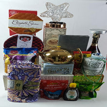 A collection of various food items and gifts arranged in a gift basket, including a golden teapot, books, and other assorted items.