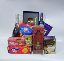 A gift basket hamper carried in a wicker basket containing savoury biscuits, wine, teas, Digestives, A box of Latte and other festive treats  