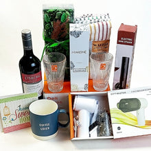A curated gift basket or bundle containing multiple items: a bottle of Eisberg wine, two ribbed drinking glasses, a white Marshé box, a striped kitchen  cloth set, an electric wine opener in its box, a gift master vacuum cleaner kit in an open box, a blue coffee lover mug, and a small decorative card.