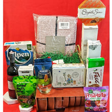 blankets, cereal, glass set, Fruitella & assorted treats around a handwoven basket against a red background