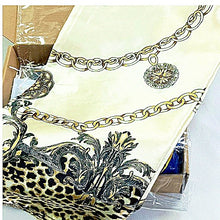 A folded scarf with a cream background, featuring a gold chain print, a black and gold baroque floral pattern, and a leopard print section, shown inside its shipping box.