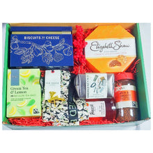 A gift hamper containing a variety of packaged food items and a silk scarf, all neatly arranged in a green box with a red ribbon.