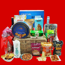 A festive Christmas basket hamper containing a variety of food items and gifts, presented on a red background.