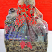 Christmas Hamper basket wrapped in tulle netting and a fancy bow. Chocolate, towels, fabrics and a few items are visible through the net.