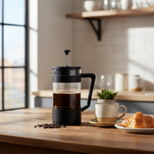 French press with coffee and a croissant on a wooden table