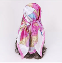 A silk scarf with a pink and white leaf pattern, styled on a mannequin head with dark brown hair against a plain white background.