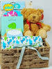 A medium blue themed handcrafted basket  with baby gifts placed in. A teddy, flannel, bath mitts, A T-rex night light and a baby photo frame. 
