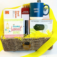 A wicker gift basket filled with assorted items, including a blue ceramic mug that reads , 'COFFEE LOVER,' a set of 4 waffle kitchen napkins a box of Deli Glass, a wine opener, a 'home Sweet HOME' card, a vacuum cleaner kit, and yellow shredded paper filler, with a bright yellow ribbon draped over the side.