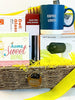 A wicker gift basket filled with assorted items, including a blue ceramic mug that reads , 'COFFEE LOVER,' a set of 4 waffle kitchen napkins a box of Deli Glass, a wine opener, a 'home Sweet HOME' card, a vacuum cleaner kit, and yellow shredded paper filler, with a bright yellow ribbon draped over the side.