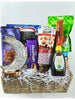 A gift basket containing a variety of snacks including cookies, cornflakes, date bars, latte, fruit juice, sparkling grape drink, incense charcoal, a rechargeable lamp, granola, honey, wax print fabric, mixed dried fruits, and chocolates.