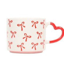White mug with red heart handle and red bow pattern on a white background