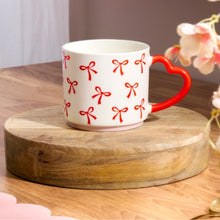 White mug with red bow patterns on a wooden coaster