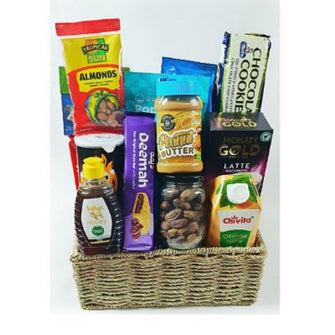 A variety of snacks and food items arranged in a wicker basket, including nuts, dates, granola, crackers, date bars, peanut butter, and other packaged snacks.