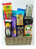 A variety of snacks and food items arranged in a wicker basket, including nuts, dates, granola, crackers, date bars, peanut butter, and other packaged snacks.