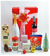 A luxury gift box containing a bottle of Veuve de Verney and Einsberg Non Alcoholic Cabernet Sauvignon, Hareem Istanbul Reed Diffuser, Cartright & Butler Rolled Oat Crumble Biscuits, Cartright & Butler Breakfast Tea, Bayara Mixed Nuts, pine cones, and berry picks, all presented against a red gift box with a decorative tree and gifts.