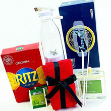 A gift basket arrangement featuring a red Ritz Crackers box, 3 green tea packets, a red tea towel with a black ribbon, a clear band white portable juicer a blue Jasmine soap box, and a fragrance diffuser bottle on a white background.