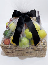 A wicker basket hamper containing an assortment of fresh fruits, tied with a black tulle netting and adorned with a black bow.