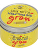Yellow tin candle inscribed Thank you for helping me grow and pencil underneath. Against a white background 